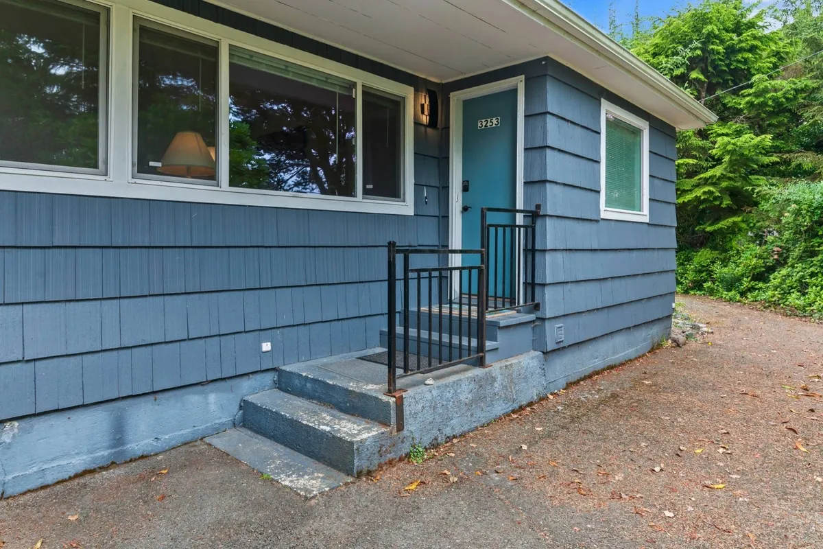 This image features the exterior of the property, including the inviting front door, steps, ramp, and several windows, all surrounded by lush greenery. The abundant trees and foliage create a secluded, peaceful vibe, hinting at the private, tree-ensconced yard mentioned in the section.
