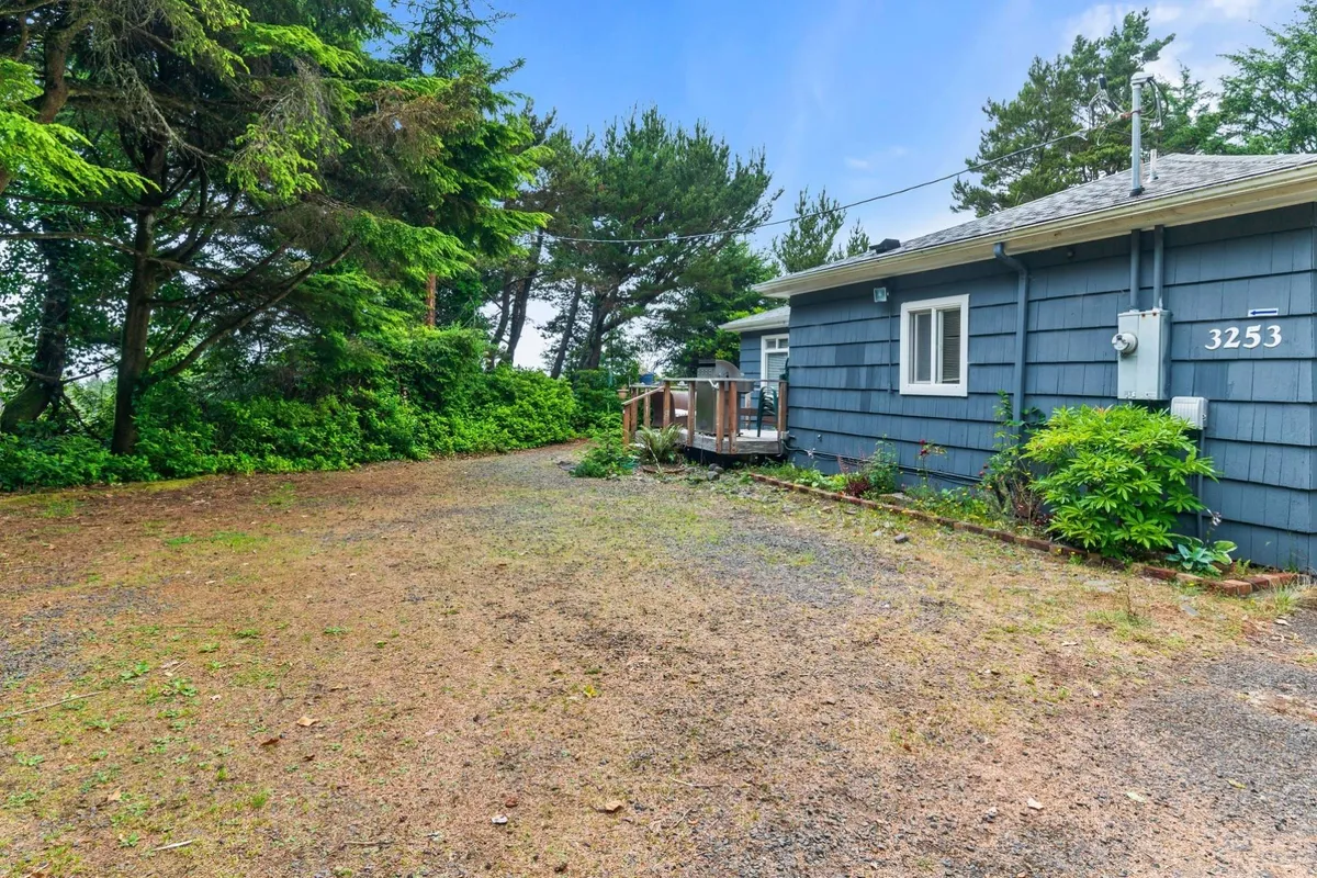 A calm, inviting exterior view of the house with a spacious deck area set against lush surrounding greenery. The deck is ideal for unwinding, socializing, and soaking up the peaceful atmosphere of the coastal setting.