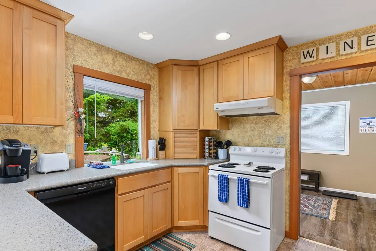 This image captures the heart of the kitchen, showcasing the cabinetry, stove, and a window view. The scene feels warm and inviting, suggesting an active cooking space where people gather, bake, and entertain. The kitchen appears spacious and functional, with natural light providing a cheerful atmosphere.