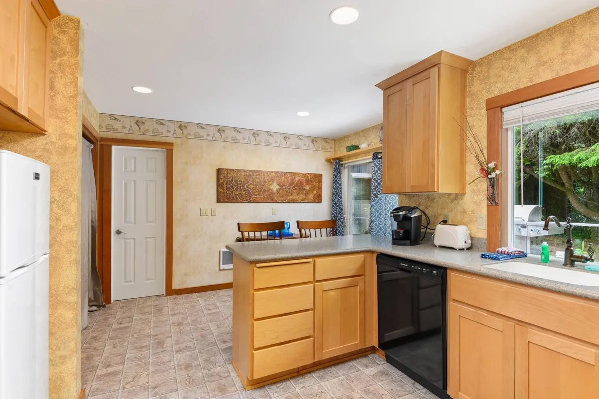 This photo focuses on a cozy kitchen island with bar stools, a window view, and a visible black dishwasher alongside wooden cabinetry. The space is ideal for casual dining, sharing recipes, and effortless meal prep, capturing the essence of a welcoming, multifunctional kitchen.