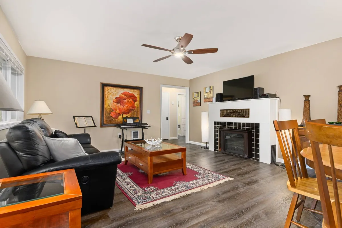 A cozy living room featuring a black leather sofa, wooden coffee table, a fireplace, and wall art. The dining table with chairs is visible, and the scene exudes warmth and comfort, inviting family members to gather, relax, and enjoy each other's company.