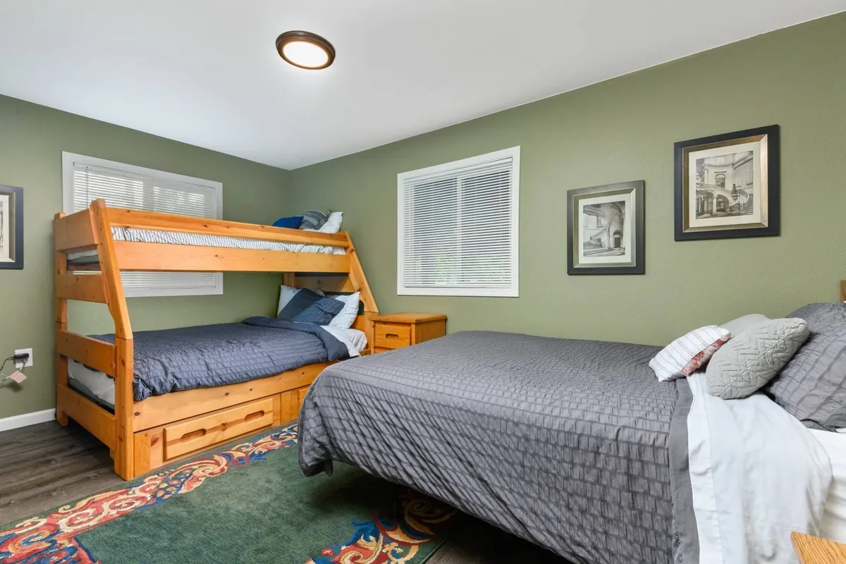 This image captures a family-friendly bedroom with a queen bed and a full-over-twin bunk bed. Playful decor and a colorful area rug make the room inviting for both children and adults. The arrangement highlights flexibility for sleeping groups of various ages.